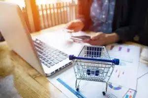 Semana do Brasil: pessoa utilizando um notebook com um carrinho de mercado em miniatura sobre a mesa.