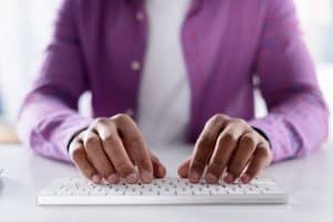 Heading tags: homem negro de camisa roxa escrevendo em teclado.
