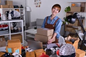 Leads qualificados para e-commerce: mulher de avental embalando produtos em uma sala com prateleiras e caixas.
