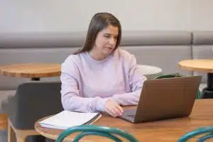 Palavras-chave no e-commerce: mulher em restaurante mexendo em notebook com caderno ao lado.