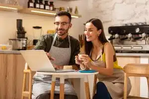 Otimize seu conteúdo do YouTube para SEO. Homem e mulher em cafeteria olhando para um notebook.