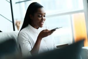 Pesquisa por voz e SEO: mulher negra gravando um áudio no celular.