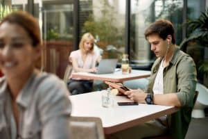 Homem sentado em cafeteria lendo em tablet.
